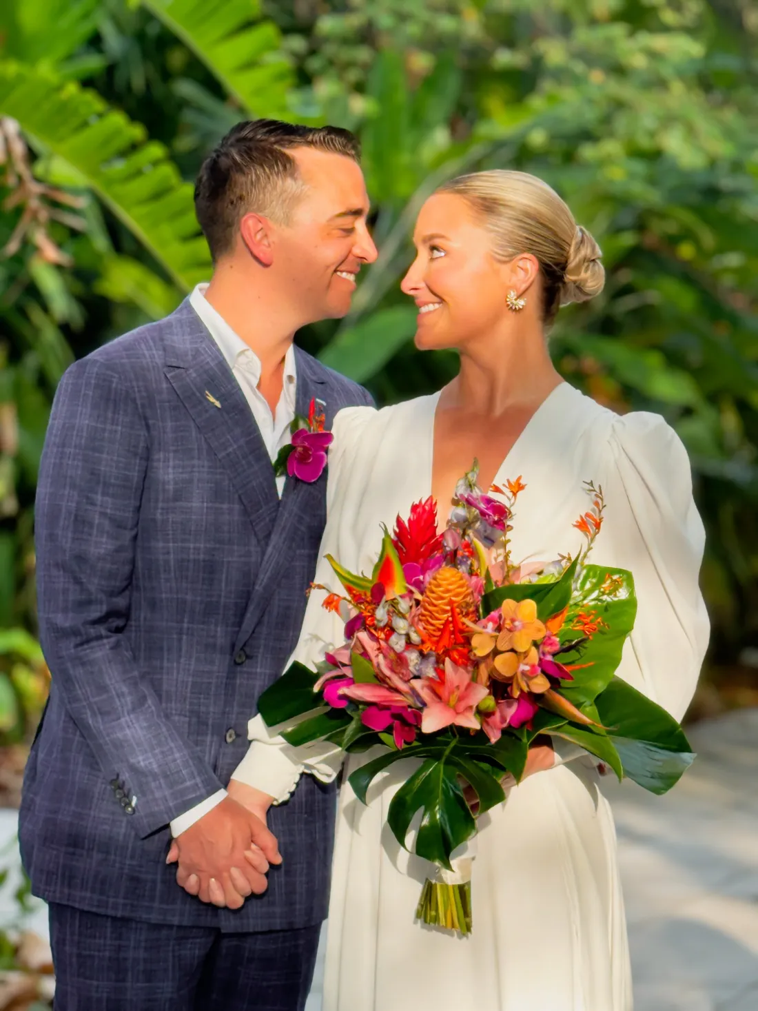 Novios con ramo tropical de heliconias, orquídeas y hojas de monstera en un jardín
