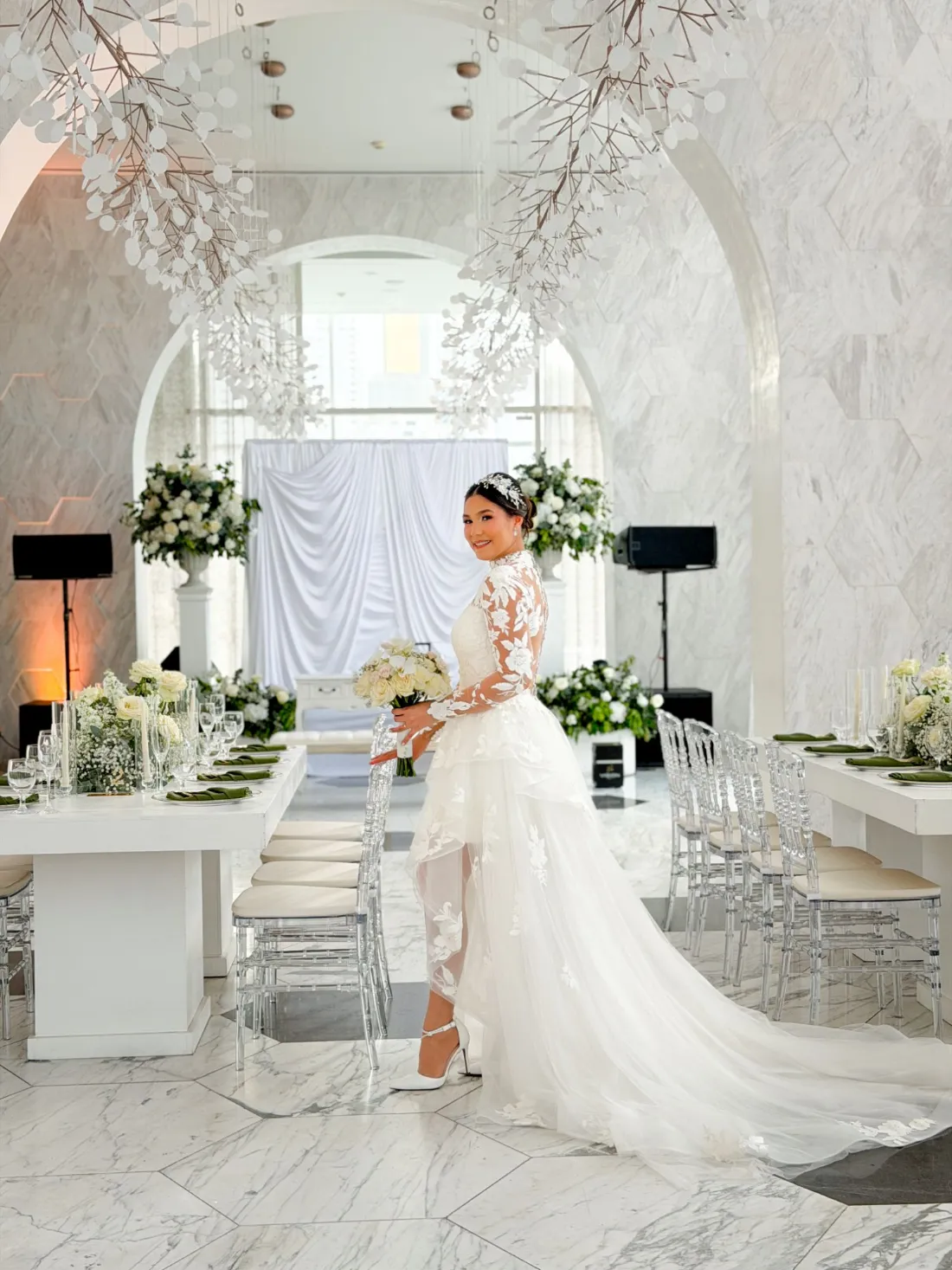 Novia en salón de mármol blanco con mesas imperiales, flores blancas y servilletas verdes