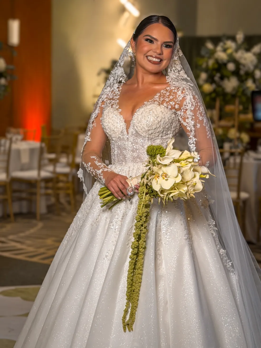 Novia con velo bordado y ramo de orquídeas blancas con amaranto colgante