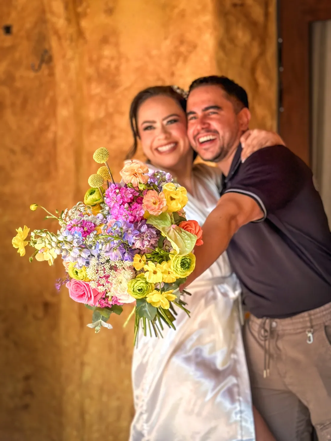 Andy Colmenares abraza a una novia con ramo multicolor de ranúnculos, delphinium y rosas